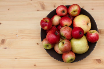 Baby and full size apples in a dish on a pine table