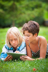 two children lying on the grass looking at something on the tabl