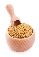 Wooden scoop in bowl full of fenugreek isolated on white