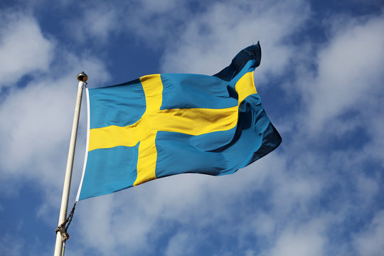 Waving swedish flag against blue sky with small white clouds