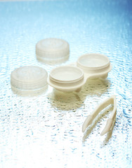 contact lenses in containers and tweezers on blue background