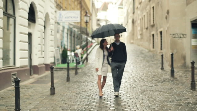 Young couple walking with umbrella in the city, steadycam shot 