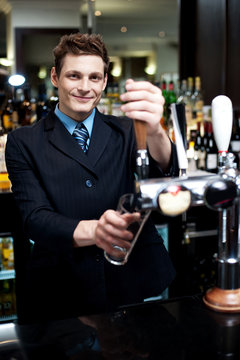 Handsome mixologist putting ice into tall glass