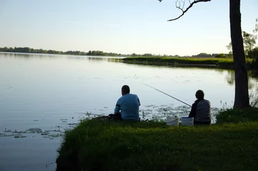 Fotobehang Man and woman sit on lake shore with rods fishing © sauletas