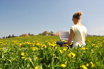 Girl with a laptop on the spring meadow