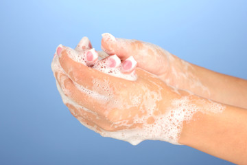 Woman's hands in soapsuds, on blue background close-up
