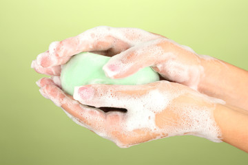 Fototapeta premium Woman's hands in soapsuds, on green background close-up