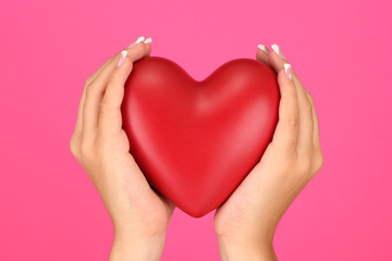 Red heart in woman's hands, on pink background close-up