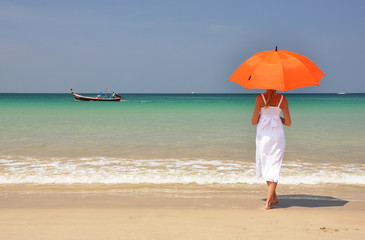 Fototapeta na wymiar Girl with an orange umbrella on the sandy beach