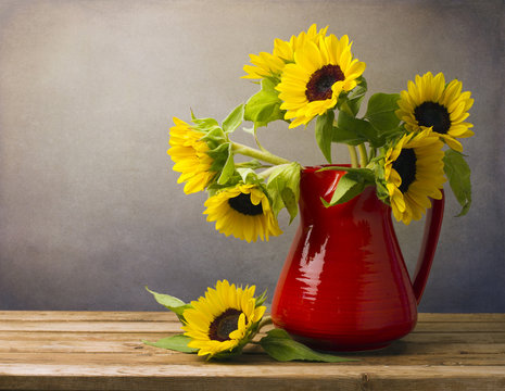 Beautiful sunflower bouquet in red jug on wooden tabletop.