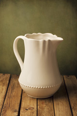 White jug on wooden table against grunge wall