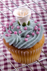 Cupcake mit blauer Buttercreme,  rosa Zuckerkugeln und einer wei