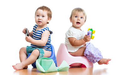 babies toddlers sitting on chamber pot and playing with toys - obrazy, fototapety, plakaty