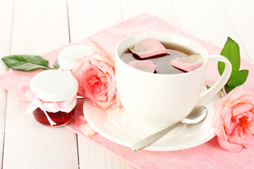 cup of tea with roses and jam on white wooden table