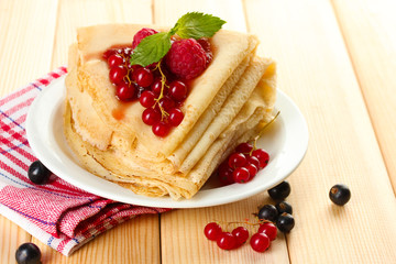 Delicious pancakes with berries and jam on plate on wooden