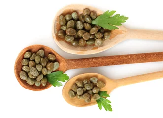 Fotobehang green capers in wooden spoons on white background close-up © Africa Studio