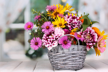 beautiful bouquet of bright flowers in basket on wooden table