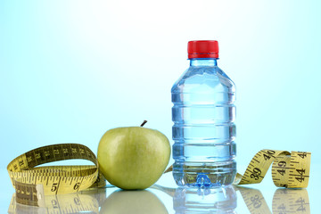 Bottle of water, apple and measuring tape on blue background