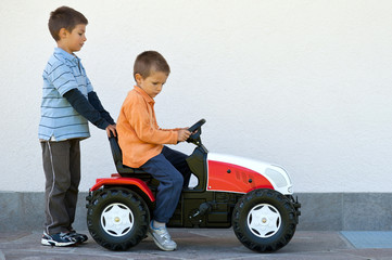 Two brothers playing with tractor toy outdoors.