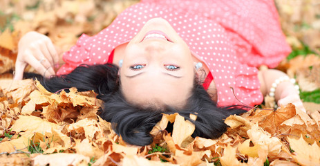 cheerful girl with blue eyes lying in autumn leaves