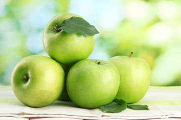 Ripe green apples with leaves, on table, on green background