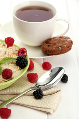 tasty oatmeal with berries and cup of tea, on white wooden