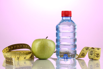 Obraz premium Bottle of water, apple and measuring tape on purple background