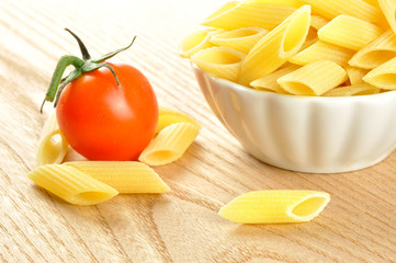 Several uncooked penne pasta and a cherry tomato, closeup