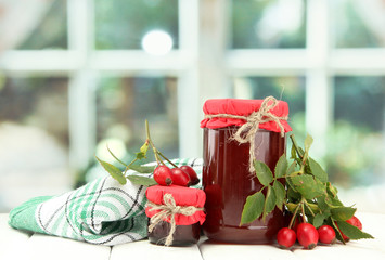 jars with hip roses jam and ripe berries, on wooden table