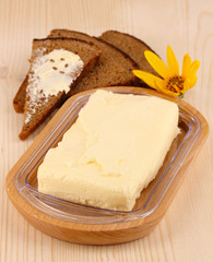 Butter on wooden holder and bread on wooden table close-up
