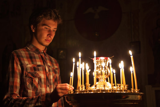 Young Man Lighting A Candle In The Church.