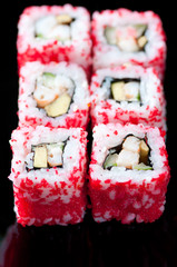 Set of California rolls on a black plate, vertical shot