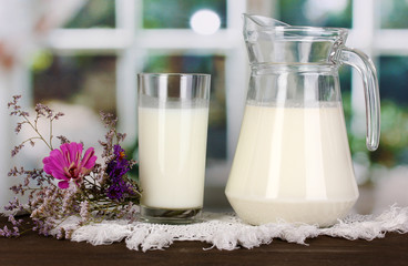 Pitcher and glass of milk on wooden table on window background