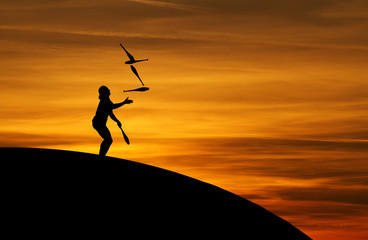 juggler in sunset with five juggling clubs