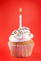 tasty birthday cupcake with candle, on red background