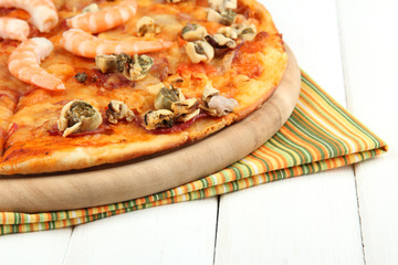 Delicious pizza with seafood on stand on wooden background