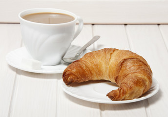a croissant and a cup of coffeee with milk.