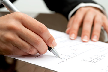 Female hand with pen pointing on accounting document.