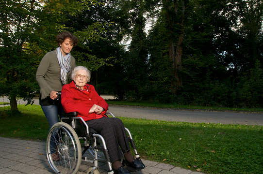 Seniorin wird im Rollstuhl von Betreuerin geschoben