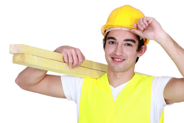 young carpenter with hand to hard hat carrying planks