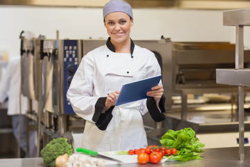 Smiling chef using her digital tablet beside the vegetables