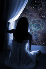 Young girl standing by the window, watching the stars