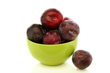 Ripe plums in green bowl.