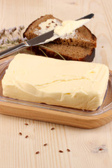 Butter on wooden holder and bread on wooden table close-up