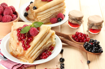 Delicious pancakes with berries, jam and honey on wooden table