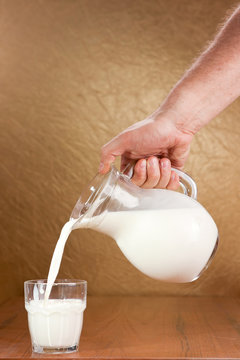 Hand pouring milk from jug to glass