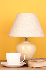 table lamp with cup and book on yellow background