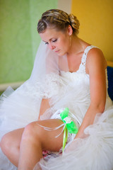 blonde bride at a wedding in the house wears a garter on the leg