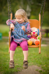 Adorable girl swing with plush toy on playground in park