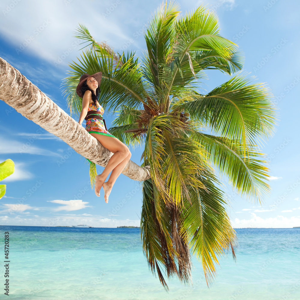 Wall mural fashion woman siting upon palm tree on the beach